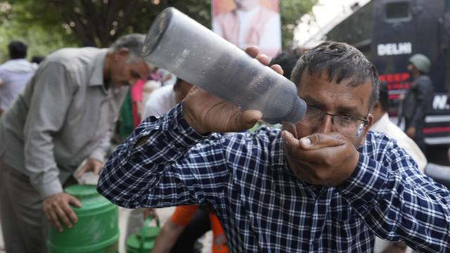 Un homme boit de l'eau à un stand en bord de route qui sert de l'eau potable gratuite alors qu'une vague de chaleur frappe la capitale indienne, New Delhi. [KEYSTONE - MANISH SWARUP]