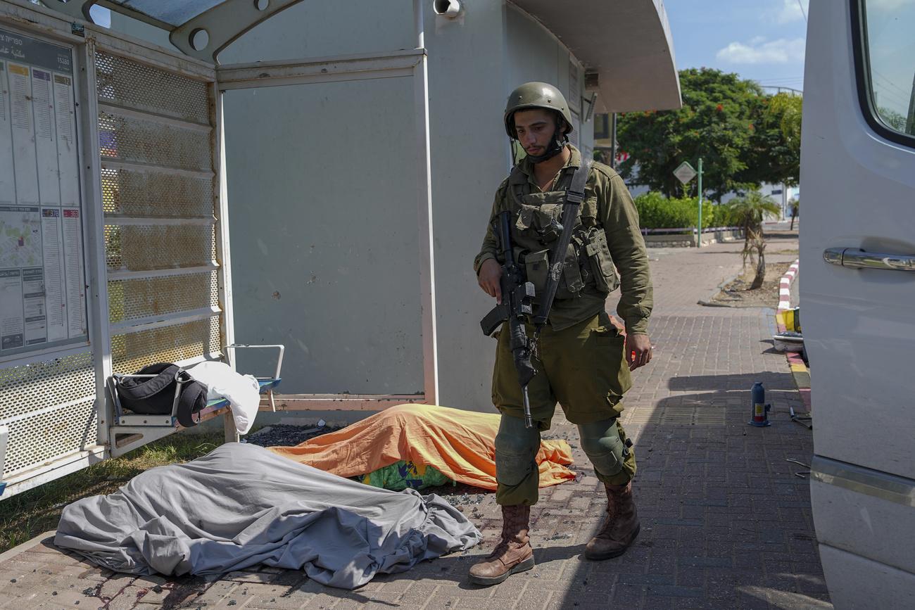 Un soldat israélien marche à côté des corps de deux personnes tuées par des combattants du Hamas, le 7 octobre à Sdérot. [KEYSTONE - TSAFRIR ABAYOV]