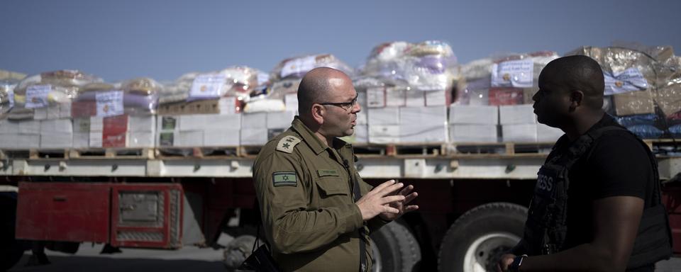 Un colonel israélien s'exprime devant des camions d'aide humanitaire bloqués pour Gaza. [Keystone/AP Photo - Maya Alleruzzo]