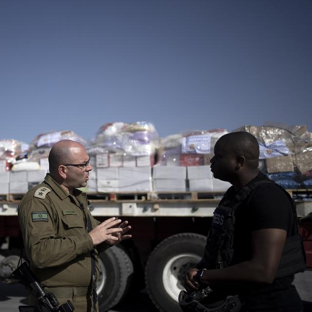Un colonel israélien s'exprime devant des camions d'aide humanitaire bloqués pour Gaza. [Keystone/AP Photo - Maya Alleruzzo]