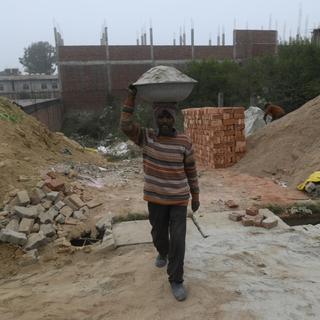 Un travailleur indien porte une bassine de ciment sur la tête. [AFP - Indranil Aditya]