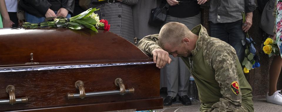 Un soldat ukrainien rend un dernier hommage au cercueil de son camarade, tué lors d'une bataille contre les troupes russes, lors de la cérémonie funéraire sur la place de l'Indépendance à Kiev, en Ukraine, le lundi 6 mai 2024. [KEYSTONE - EFREM LUKATSKY]