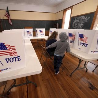 Une femme, accompagnée de son fils, dans un bureau de vote. 5 novembre 2024. [AP Photo/Keystone - Charlie Riedel]