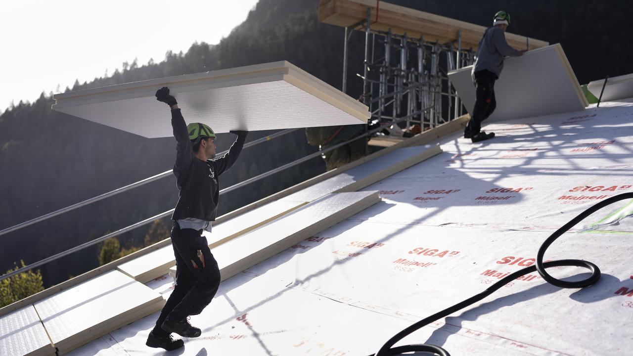 Les ouvriers du bâtiment de Greencover AG transportent et distribuent des panneaux isolants sur le toit, photographiés le mercredi 6 novembre 2024 à Pfaefers, dans le canton de Saint-Gall. La modernisation de l'isolation du toit contribue à la rénovation énergétique d'un bâtiment et donc également à la réduction des gaz à effet de serre (image d'illustration). [keystone - Gaetan Bally]