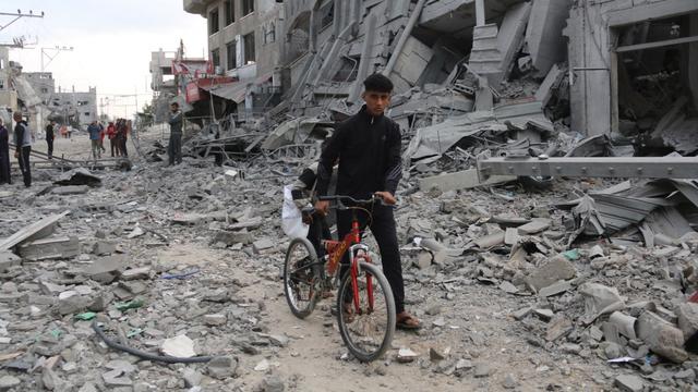 Un jeune Palestinien marche en poussant son vélo au milieu des décombres après des frappes israéliennes dans le camp de réfugiés de Nuseirat, dans le centre de la bande de Gaza, le 1er novembre 2024. [AFP - EYAD BABA]