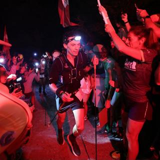 Le coureur américain Jim Walmsley est accueilli par des supporters munis de fusées éclairantes lors de l'ascension de Notre-Dame-de-la-Gorge pendant l'Ultra-trail du Mont Blanc (UTMB) aux Contamines-Montjoie, le 30 août 2024. [AFP - EMMANUEL DUNAND]