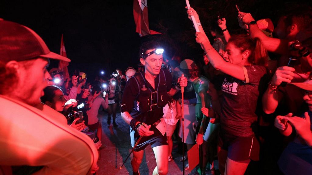 Le coureur américain Jim Walmsley est accueilli par des supporters munis de fusées éclairantes lors de l'ascension de Notre-Dame-de-la-Gorge pendant l'Ultra-trail du Mont Blanc (UTMB) aux Contamines-Montjoie, le 30 août 2024. [AFP - EMMANUEL DUNAND]