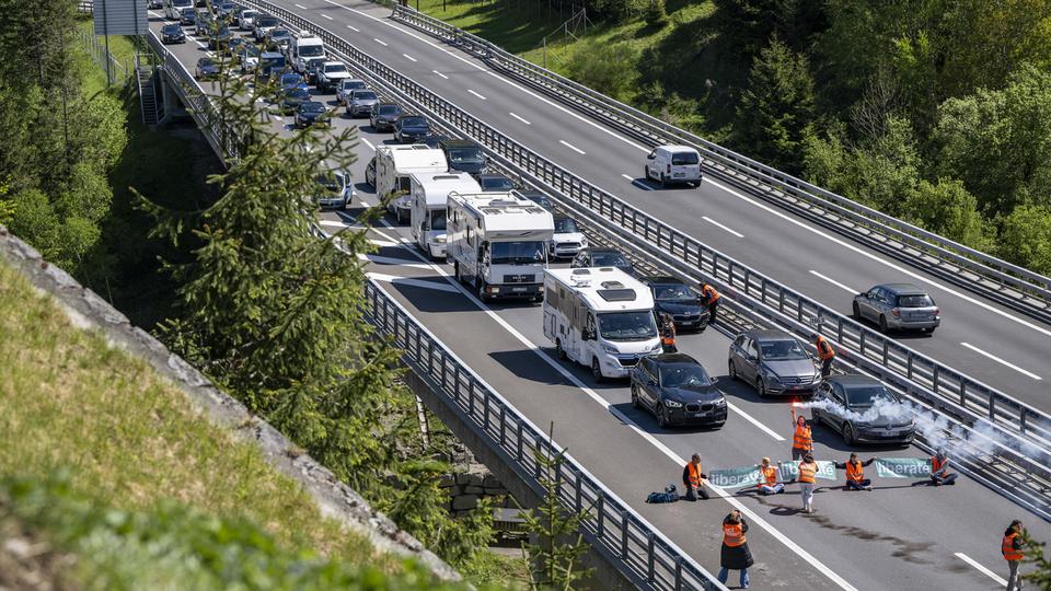 Des activistes de "Renovate Switzerland" protestent devant le tunnel du Gothard près de Goeschenen dans le canton d'Uri, pendant que le trafic voyageurs de l'Ascension est bloqué sur plusieurs kilomètres devant le portail nord du Gothard, le jeudi 9 mai 2024 à Wassen. [KEYSTONE - URS FLUEELER]