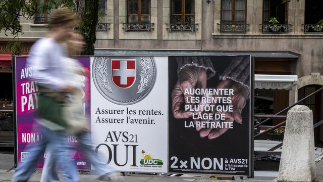 Des personnes passent devant les affiches des partis politiques et des associations donnant leurs mots d'ordre pour les votations féderales du 25 septembre. [KEYSTONE - MARTIAL TREZZINI]