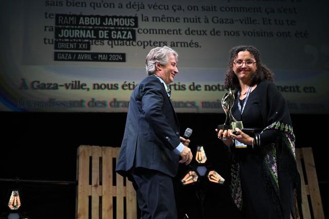 La rédactrice en cheffe d'Orient XXI, Sarra Grira, reçoit le trophée récompensant Rami Abou Jamous pour son travail de correspondant de guerre à Gaza. [AFP - LOU BENOIST]