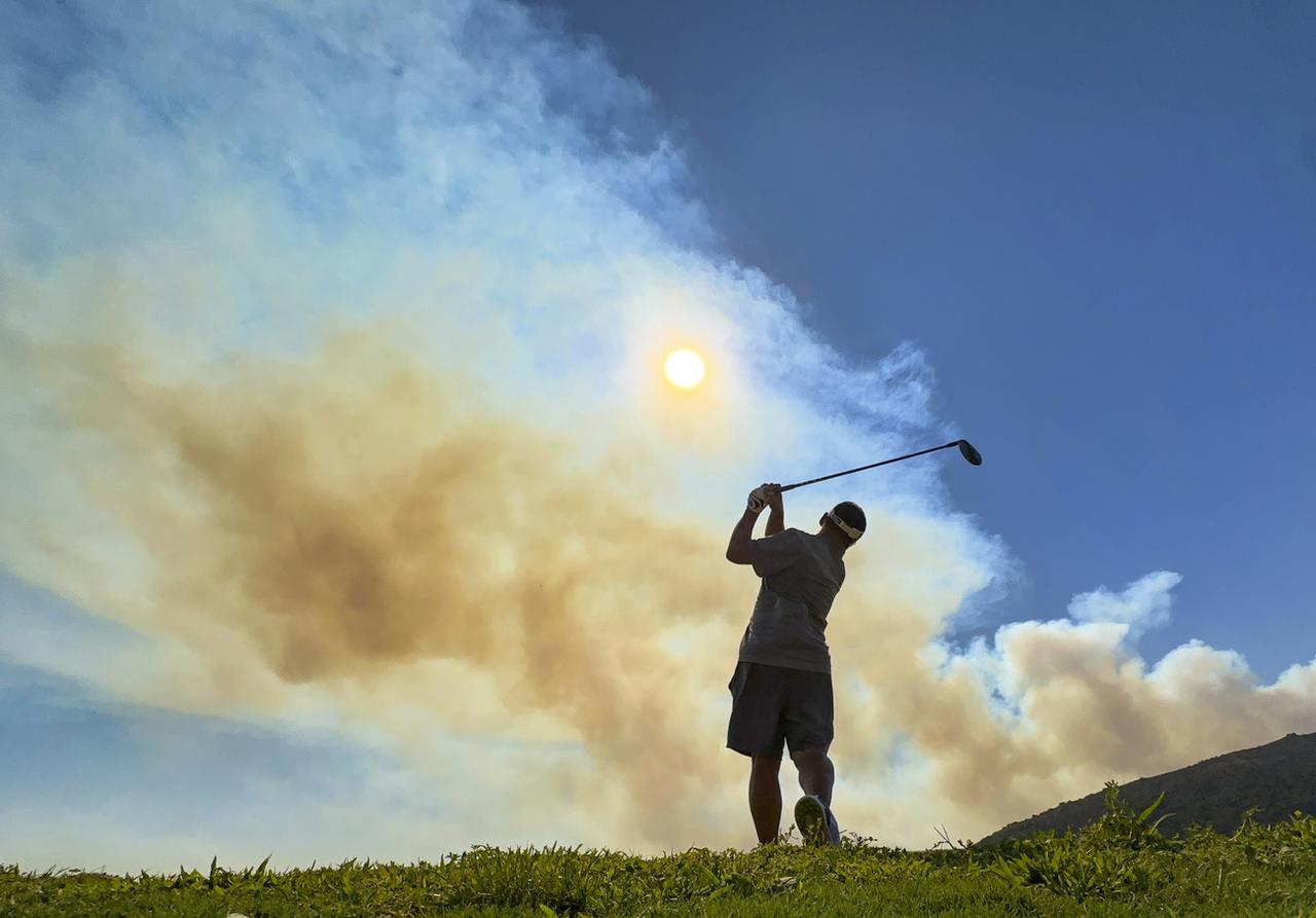 Un homme joue au golf à Corona, alors que de la fumée liée à l'Airport Fire s'élève dans le ciel californien. [KEYSTONE - JEFF GRITCHEN]