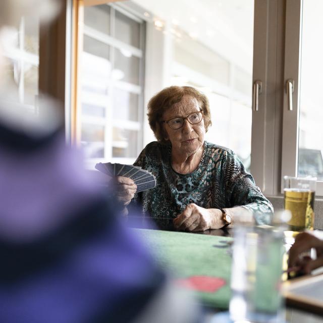 Une femme âgée jouant au cartes avec d'autres seniors. [Keystone - Gaetan Bally]