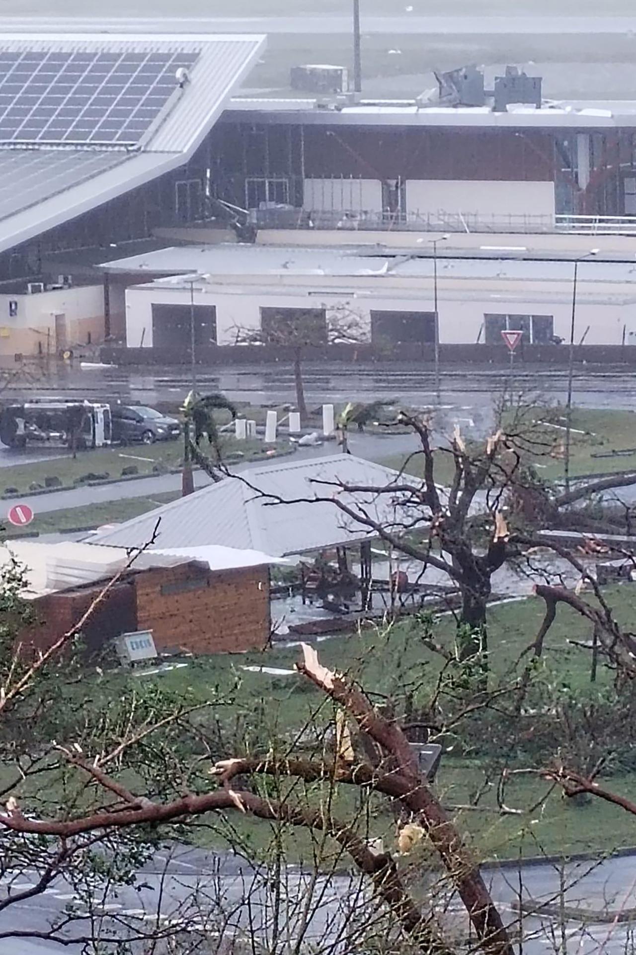 Cette photo prise et diffusée par la Direction générale de l'aviation civile le 14 décembre 2024 montre des arbres cassés et une voiture retournée à l'aéroport international Marcel Henry de Dzaoudzi-Pamandzi, quelques heures après le passage du cyclone Chido. [AFP - HANDOUT]