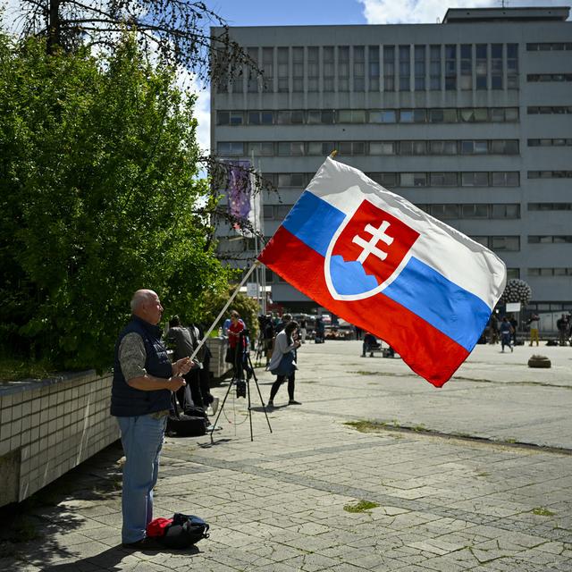 Un homme tient un drapeau de la Slovaquie devant le F. D. Roosevelt University Hospital où est soigné le Premier ministre Robert Fico. [AP Photo/Keystone - Denes Erdos]