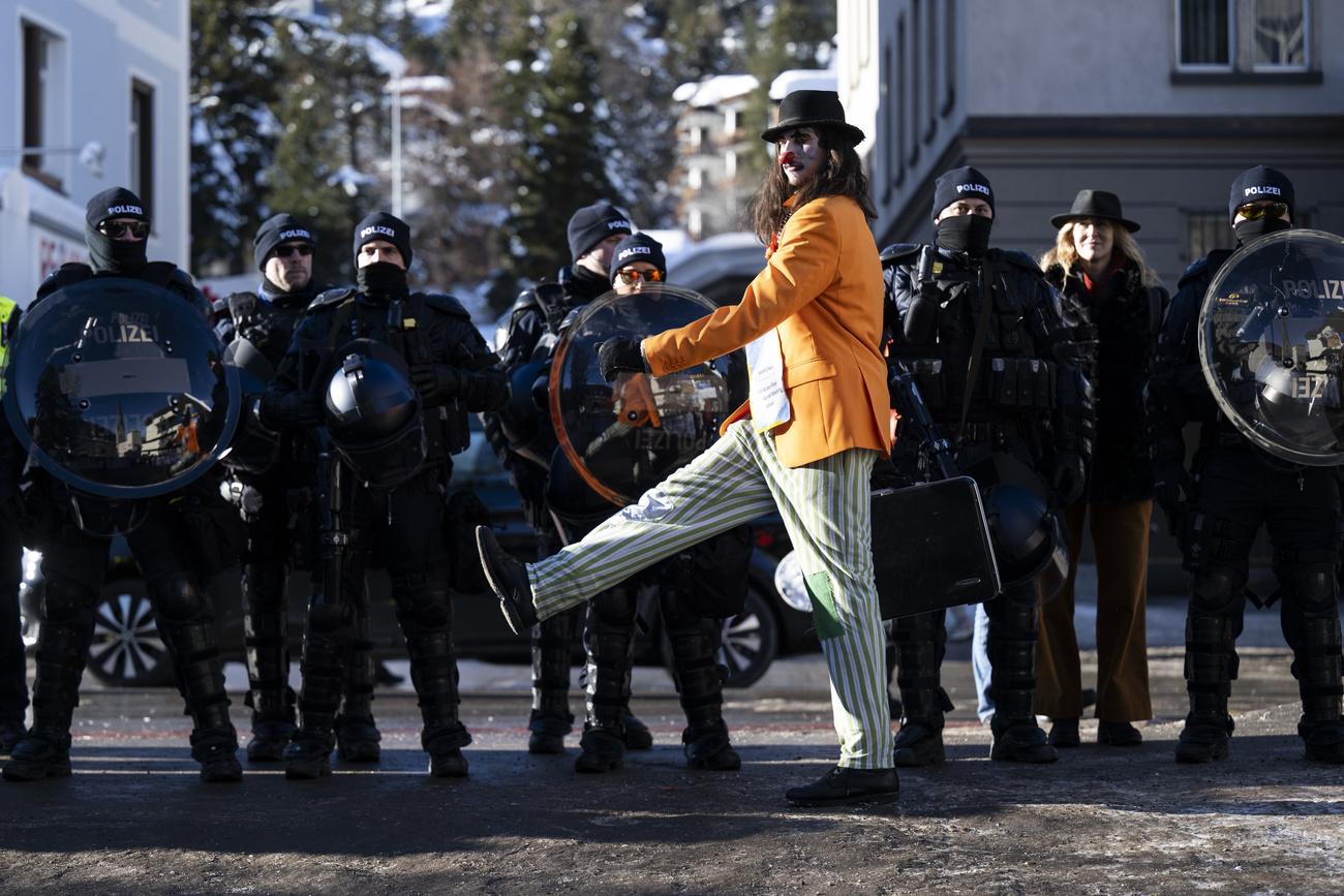 Un manifestant déguisé en clown devant un cordon policier dans la station grisonne de Davos, la veille de l'ouverture du WEF. [Keystone - Laurent Gillieron]