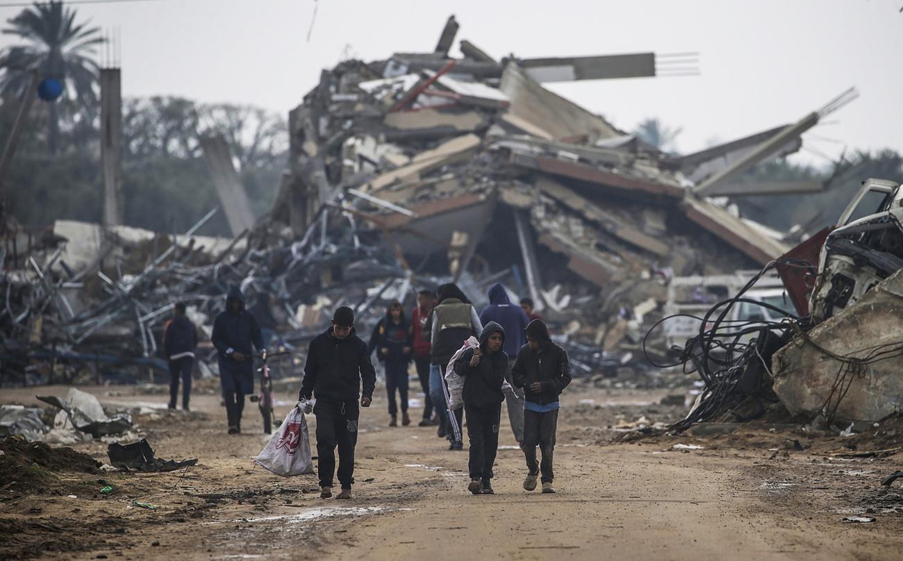 Des Palestiniens passent devant les décombres de structures détruites lors d'une opération militaire israélienne dans le camp de réfugiés d'Al Nusairat, le 19 février 2024. [KEYSTONE - MOHAMMED SABER]