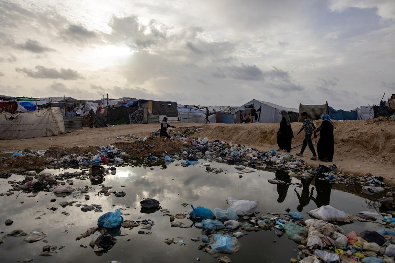 Des Palestiniens marchent à côté des ordures dans un camp de déplacés à Rafah, le 26 avril. [KEYSTONE - HAITHAM IMAD]