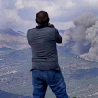 Un adulte et un enfant regardent de la fumée après des tirs israéliens au sud du Liban. [Keystone/AP Photo - Hussein Malla]