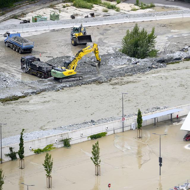 Des pelleteuses dégagent le gravier qui a remonté le niveau de la rivière après les récentes inondations causées par le débordement du Rhône sur le plateau en Valais. [Keystone - Jean-Christophe Bott]