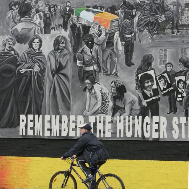 Un jeune à vélo devant un mur en hommage à l'IRA. [Keystone/EPA - PAUL MCERLANE]