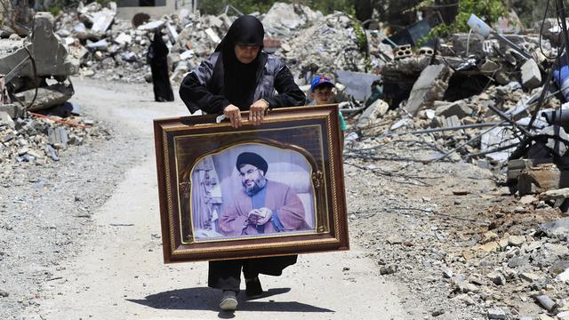 Une femme avec le portrait du chef du Hezbollah Sayyid Hassan Nasrallah se promène dans les ruines du village libanais détruit par des tirs aériens israéliens à Aita al-Shaab. [Keystone/AP Photo - Mohammed Zaatari]