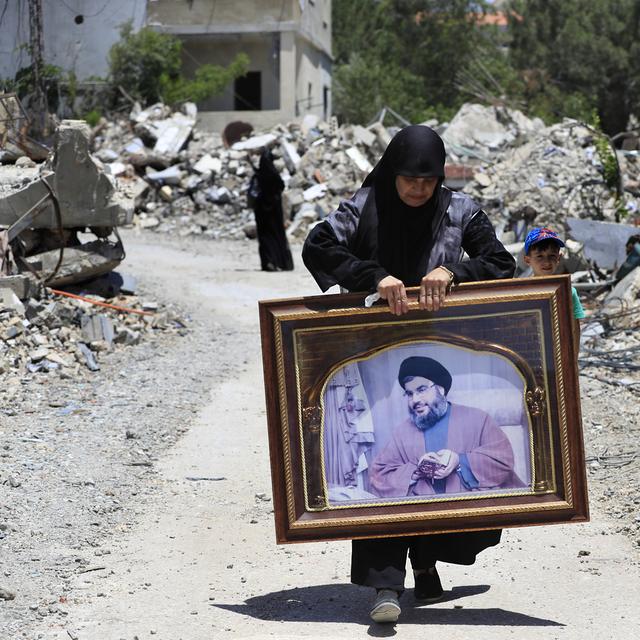 Une femme avec le portrait du chef du Hezbollah Sayyid Hassan Nasrallah se promène dans les ruines du village libanais détruit par des tirs aériens israéliens à Aita al-Shaab. [Keystone/AP Photo - Mohammed Zaatari]