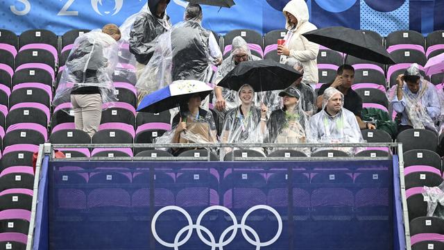 Des spectateurs attendent la cérémonie d'ouverture des JO de Paris sous la pluie. [Pool Photo via AP/Keystone - Loic Venance]