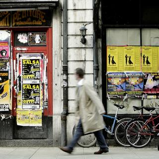 Une personne passe devant des vitrines recouvertes d'affiches sauvages a la rue de Lausanne [Keystone - Salvatore di Nolfi]