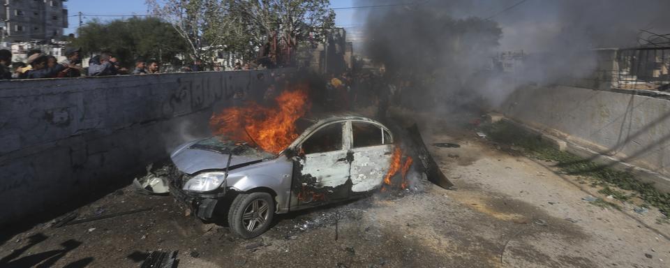 Une voiture brûle après avoir été touchée par une frappe israélienne à Gaza. [Keystone - AP Photo/Hatem Ali]