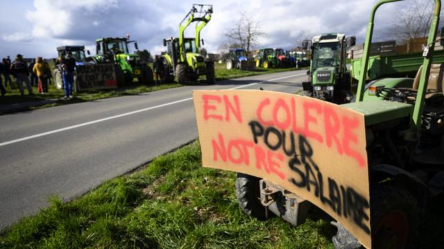 Des tracteurs avec des slogans stationnes le long de la route pendant l'action "Feu de protestation pour l'agriculture" lancée par le groupe Facebook "Révolte agricole Suisse" lors le 24 fevrier 2024 à Lussy-sur-Morges. [keystone - Laurent Gillieron]