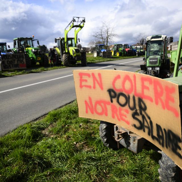 Des tracteurs avec des slogans stationnes le long de la route pendant l'action "Feu de protestation pour l'agriculture" lancée par le groupe Facebook "Révolte agricole Suisse" lors le 24 fevrier 2024 à Lussy-sur-Morges. [keystone - Laurent Gillieron]