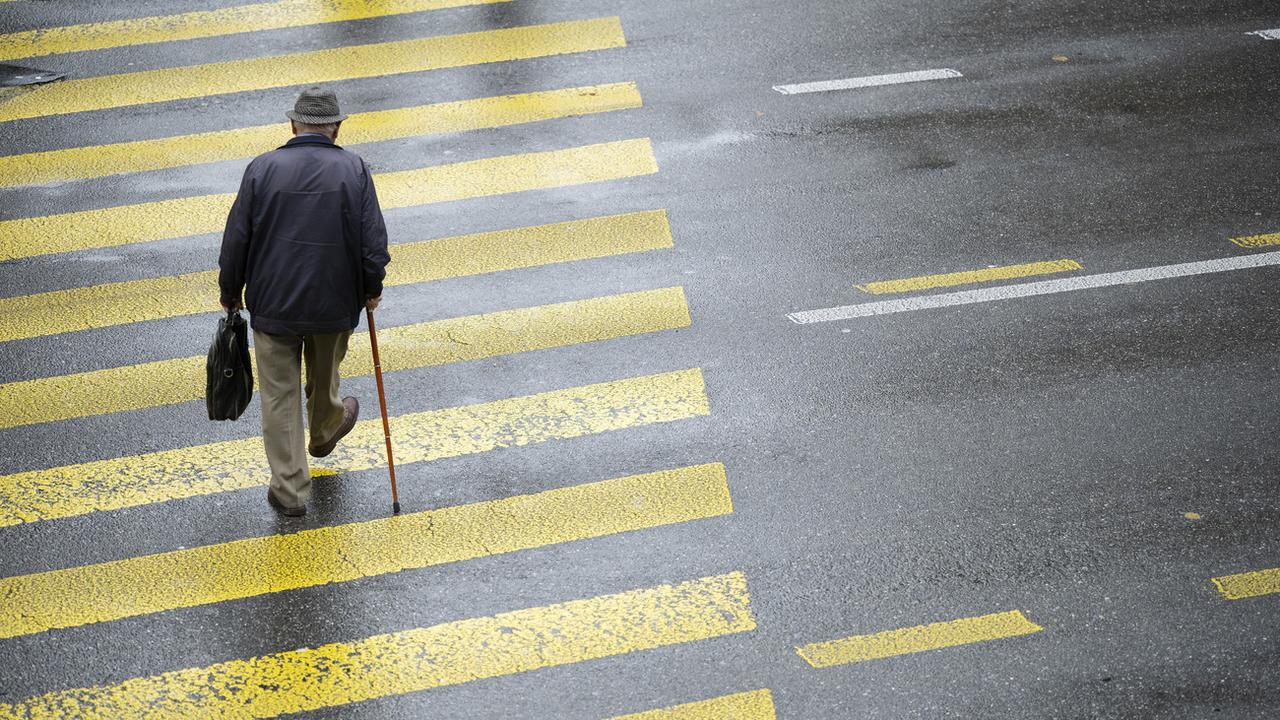 Un vieil homme avec une canne traverse la rue sur un passage piéton. [Keystone - Christian Beutler]