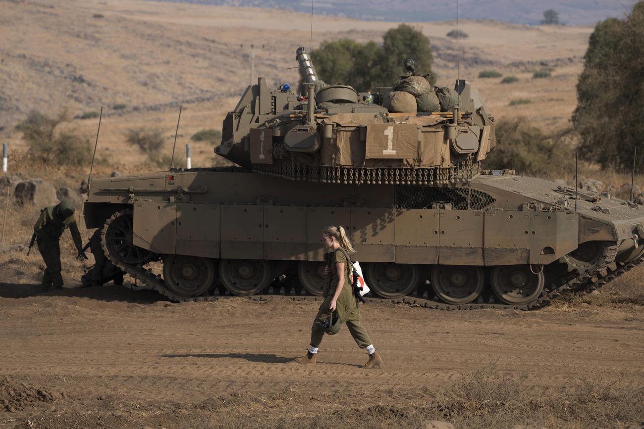 Une soldate passe devant un tank de l'armée israélienne, le 14 octobre 2023, à proximité de la frontière avec le Liban. [KEYSTONE - PETROS GIANNAKOURIS]