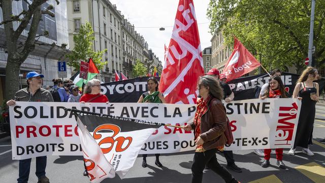 Des manifestants avec des pancartes et des drapeaux défilent dans les rues de Genève, lors du défilé du 1er mai 2024. [Keystone - Martial Trezzini]