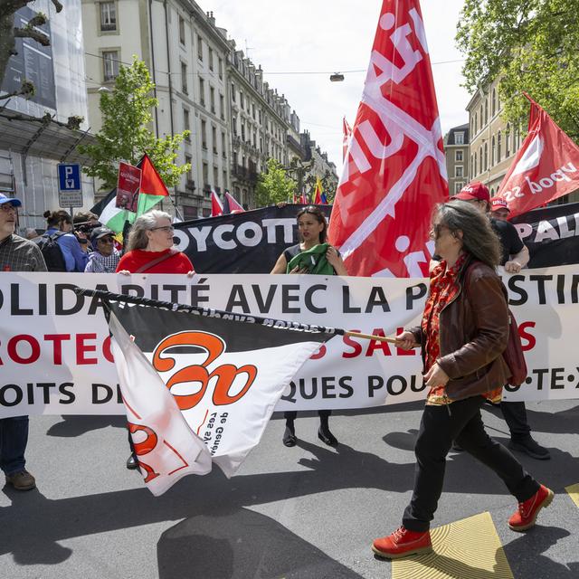 Des manifestants avec des pancartes et des drapeaux défilent dans les rues de Genève, lors du défilé du 1er mai 2024. [Keystone - Martial Trezzini]