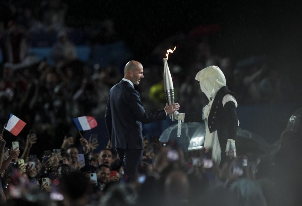 L'homme masqué remettant la flamme olympique à Zinedine Zidane lors de la cérémonie d'ouverture des JO à Paris, le 26 juillet 2024. [Anadolu via AFP - MUSTAFA CIFTCI]