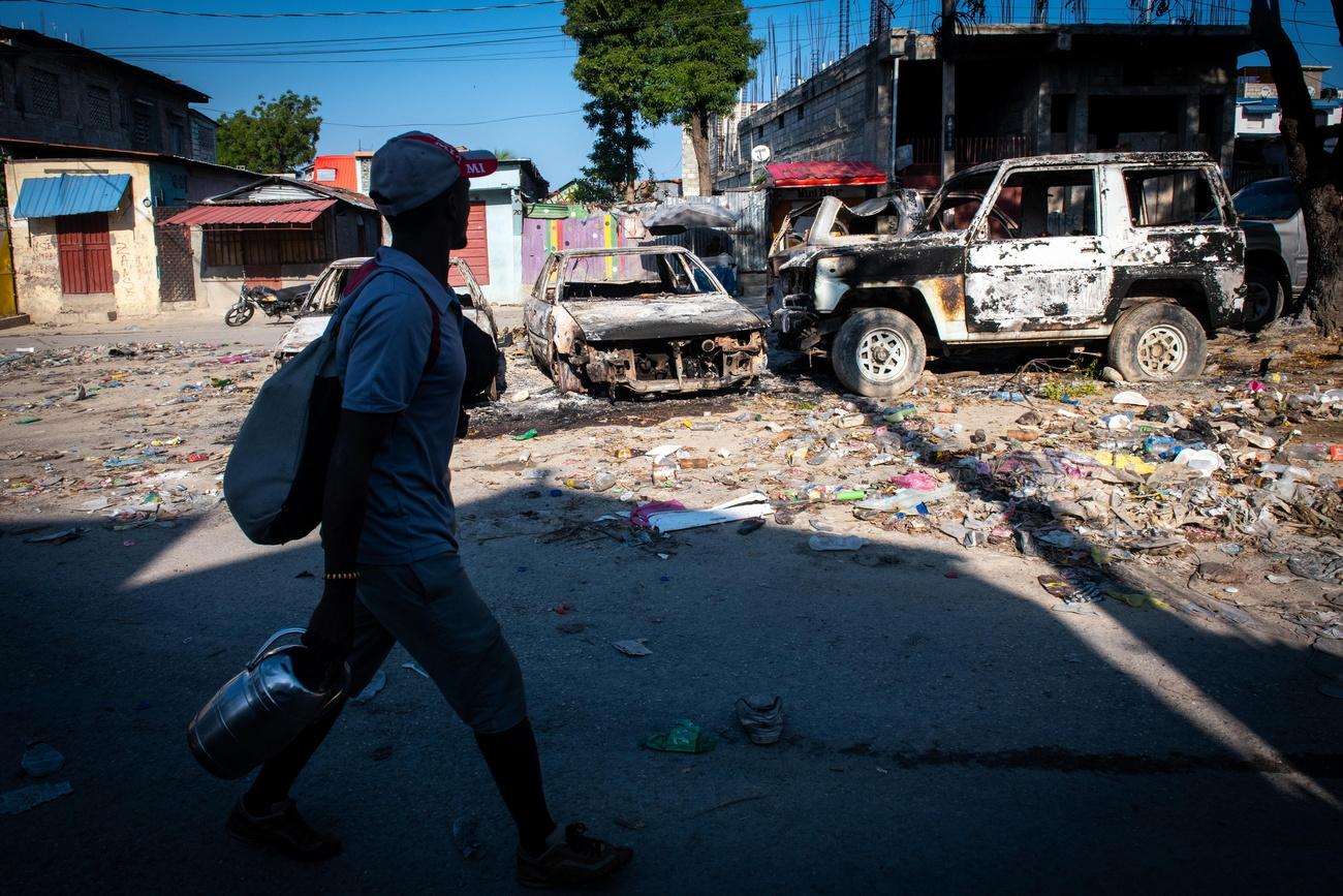 Un homme marche devant des véhicules brûlés suite à des violences à Port-au-Prince, en Haïti, le 9 mars 2024. [KEYSTONE - JOHNSON SABIN]