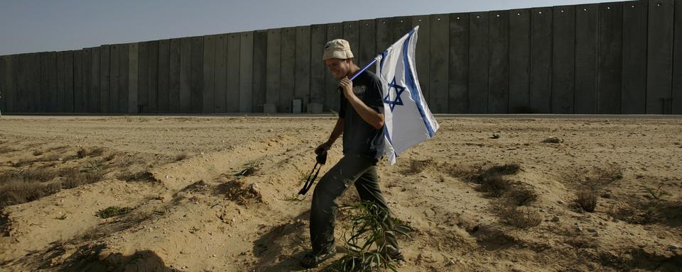 Un colon juif porte un drapeau israélien lors d'une manifestation le long de la barrière près de Netiv Ha'Asara, à la frontière avec la bande de Gaza, dans le sud d'Israël, le 26 juillet 2007. [Keystone - AP Photo/Ariel Schalit]