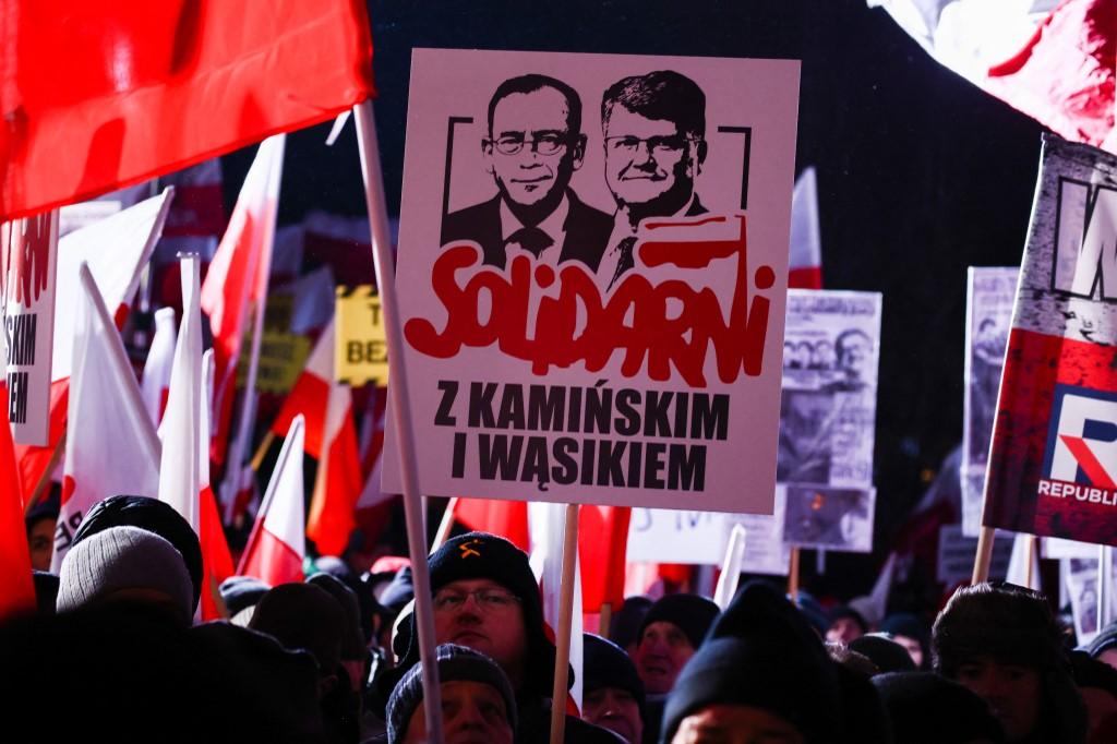 Un protestataire porte une pancarte en soutien à Mariusz Kaminski (gauche) et Maciej Wasik lors d'une manifestation contre le nouveau gouvernement pro-européen de la Pologne, le 11 janvier 2024. [NURPHOTO via AFP - BEATA ZAWRZEL]