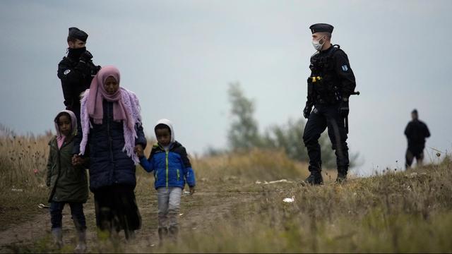 Des policiers encadrent une femme migrante et ses deux enfants près de Calais en France. [Keystone/AP Photo - Christophe Ena]