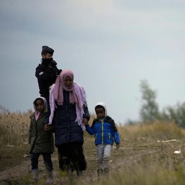 Des policiers encadrent une femme migrante et ses deux enfants près de Calais en France. [Keystone/AP Photo - Christophe Ena]