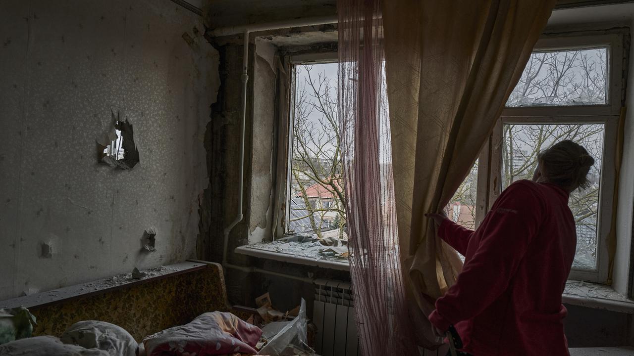 Une femme ukrainienne regarde à travers la fenêtre de son appartement bombardé. [Keystone/AP Photo - LIBKOS]