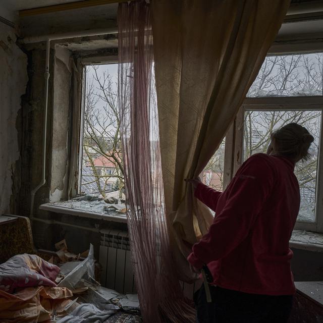 Une femme ukrainienne regarde à travers la fenêtre de son appartement bombardé. [Keystone/AP Photo - LIBKOS]