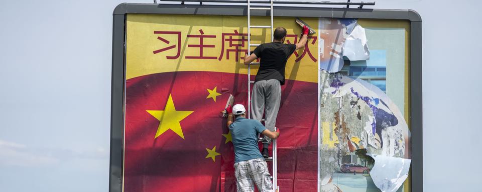 Des ouvriers qui installent un drapeau chinois à Belgrade. [Keystone/AP Photo - Darko Vojinovic]