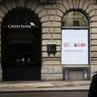 People sit in front of a logo of Swiss bank Credit Suisse, left, next to a screen showing a logo of Swiss Bank UBS and the logo of Swiss Football Association SFV with the words "A bank like Switzerland" at Zurich's Paradeplatz on Monday, June 10, 2024 in Zurich, Switzerland. [Keystone - Michael Buholzer]