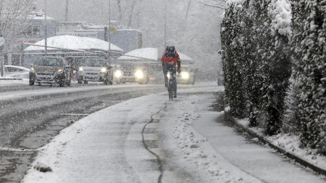 Cycliste et autos à Genève, où la neige tombe dru. [Keystone - Salvatore Di Nolfi]