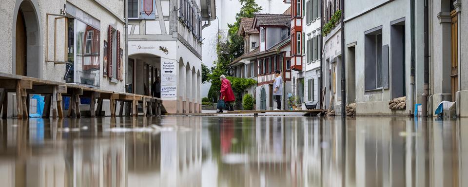 Deux femmes passent un pont temporaire sur la rive du Lac de Constance en pleine crue. [Keystone - Michael Buholzer]