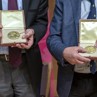 Laureats du prix Nobel de physique Didier Queloz, gauche, et Michel Mayor, droite, presentent leurs medailles a la presse, apres leur descentes de l'avion qui les ramene de Stockholm en suede, ce samedi 14 decembre 2019 a l'aeroport international de Geneve (AIG). [Keystone - Martial Trezzini]