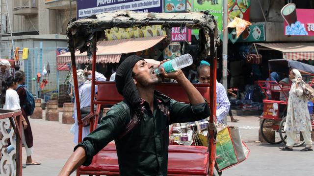 Un conducteur de rickshaw boit de l'eau pendant la canicule dans les vieux quartiers de Delhi, le 22 mai 2024. [KEYSTONE - RAJAT GUPTA]