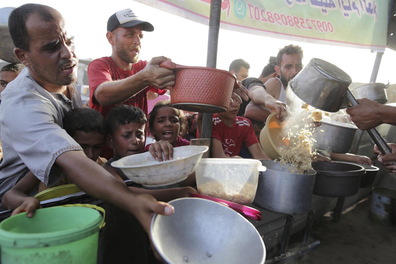Des adultes et des enfants palestiniens lors d'une distribution de nourriture, la veille de l'Eid al-Adha, le 15 juin 2024. [KEYSTONE - JEHAD ALSHRAFI]